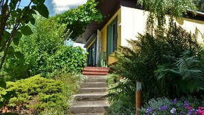 Ein Haus mit einer Steintreppe, die zu einer grünen Tür führt, umgeben von üppiger Vegetation und blühenden Pflanzen.