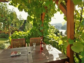 A wooden table with a bottle of red wine, two glasses, and a tray with three small items. - Holiday Home Lake View (Unterwellenborn)
