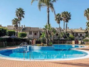 A swimming pool with a tiled deck, surrounded by palm trees and a building with a tiled roof. - Belvilla by OYO Holiday Home in Rota (Rota)