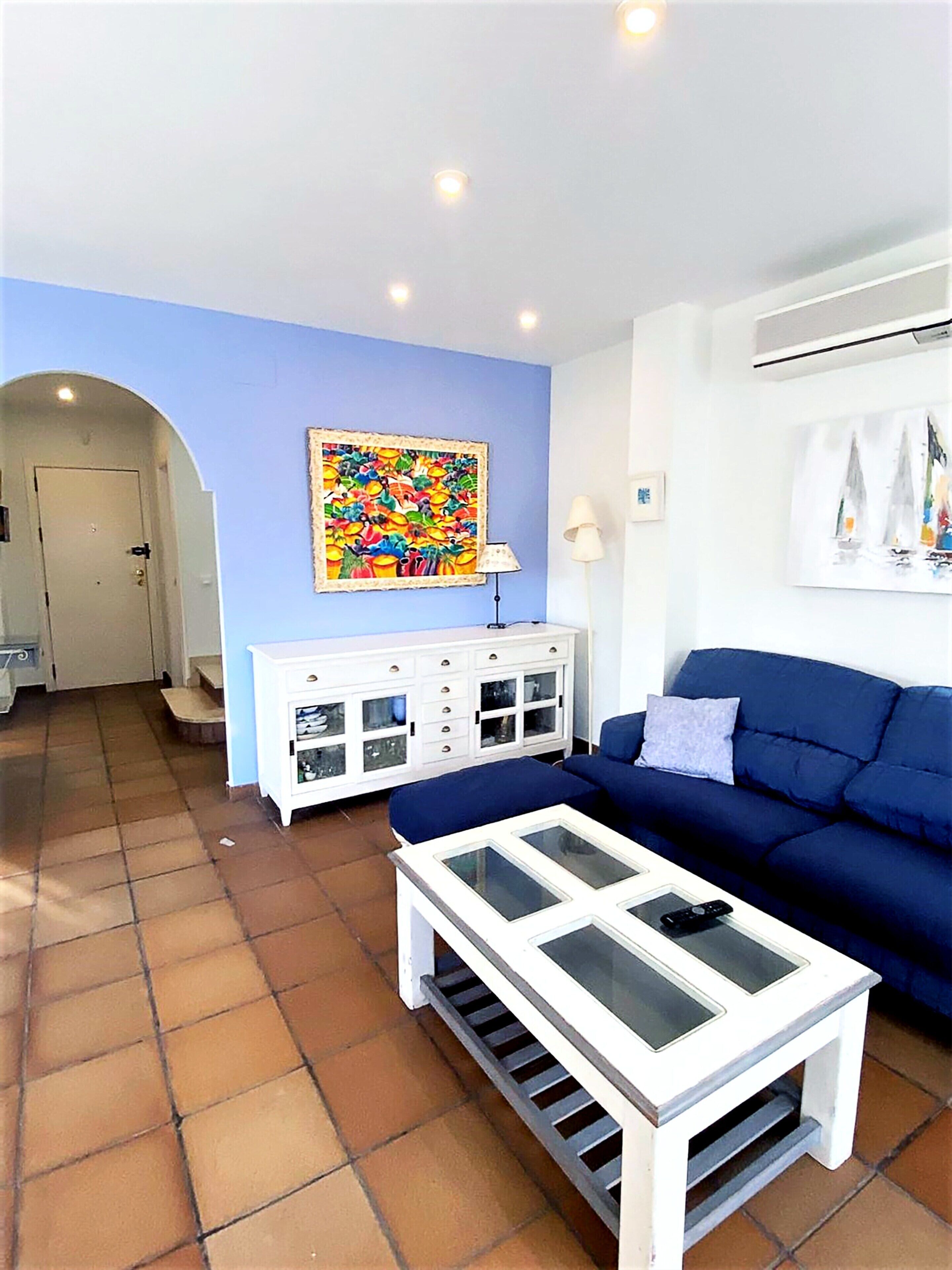 A living room with a blue sofa, a white cabinet, and a colorful painting on the wall.