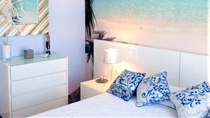 A bedroom with a bed, a nightstand, a lamp, and a wall mural of a beach scene. - Belvilla by OYO Holiday Home in Rota (Rota)