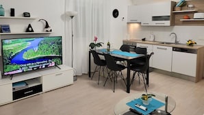 Una sala de estar moderna con televisión de pantalla plana, mesa de comedor, sillas y una cocina con armarios y lavamanos.