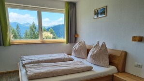 A bedroom with a wooden bed, a nightstand, a window with a view of mountains, and a small painting on the wall. - Flat in Wagrain Near Ski Slopes (Wagrain)