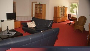 Un salon avec un canapé en cuir noir, un meuble en bois, un téléviseur et une moquette rouge.