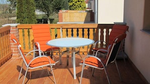 Eine Holzterrasse mit einem runden Tisch und vier orangefarbenen Stühlen.