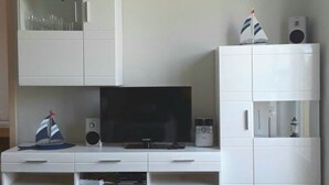 Ein modernes Wohnzimmer mit Flachbildfernseher, weißen Schränken und einer kleinen Segelboot-Dekoration.