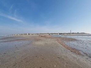 A beach with a clear sky, sandy shore, and a distant hill with a structure. - 4 Star Holiday Home in Blavand (Blavand)