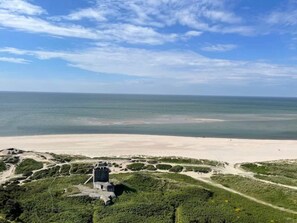 A coastal landscape with a sandy beach, a clear sky, and a structure with a dark roof. - 4 Star Holiday Home in Blavand (Blavand)