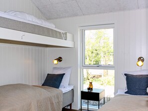 A room with bunk beds, a small table with a vase, and two wall-mounted lamps.
