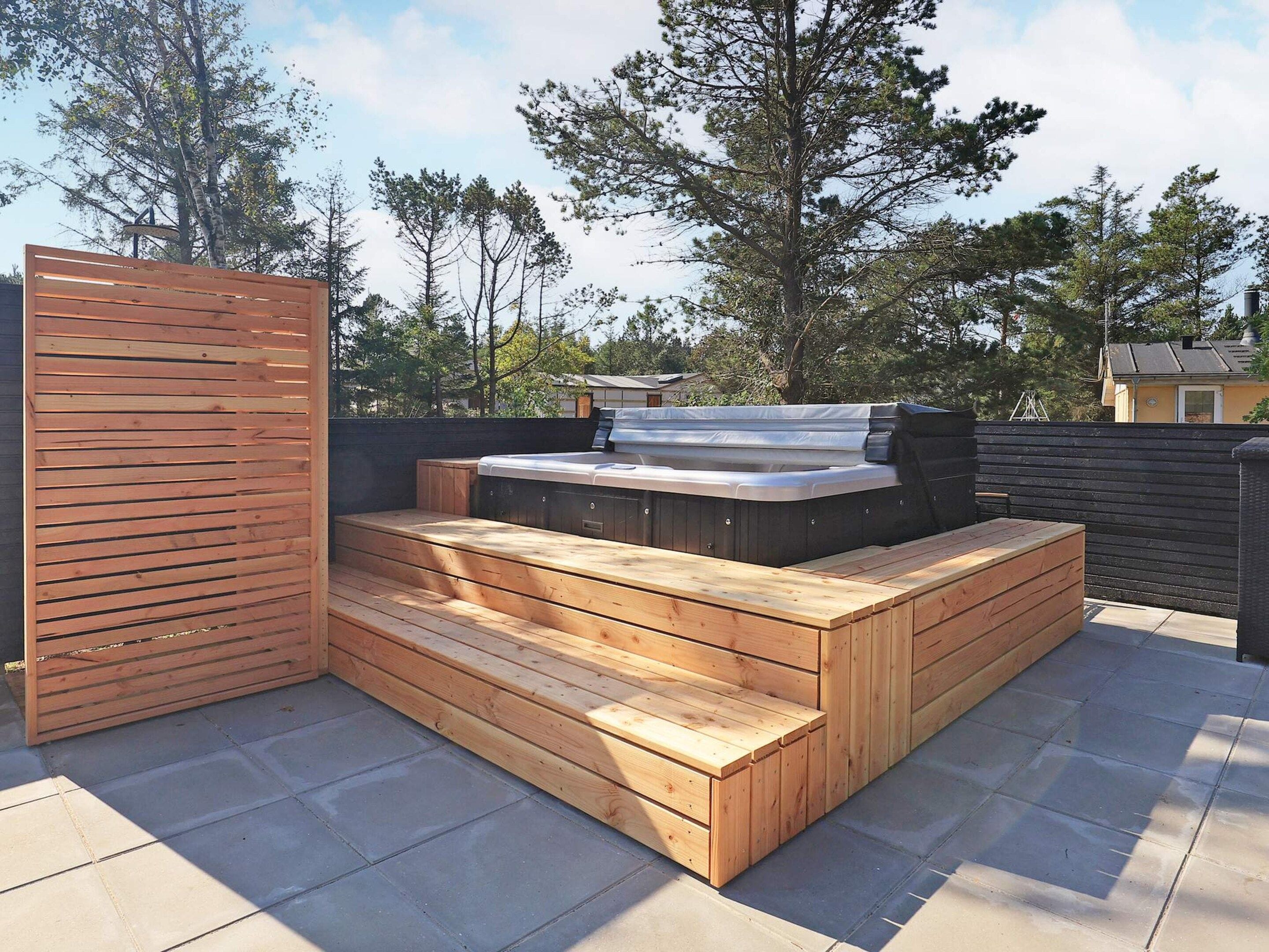 Una terraza en la azotea con jacuzzi, asientos de madera y vistas a los árboles circundantes.