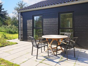 A modern outdoor patio with a round table and four chairs, surrounded by a black wooden wall with large windows. - 4 Star Holiday Home in Blavand (Blavand)