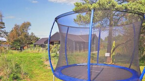 Un trampoline doté d’un filet de sécurité, installé dans un espace herbeux, avec des maisons en arrière-plan.