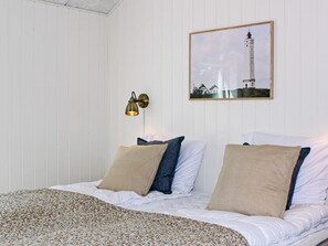 A neatly made bed with a floral-patterned bedspread, a wall-mounted picture of a lighthouse, and a wall sconce with a warm light. - 4 Star Holiday Home in Blavand (Blavand)