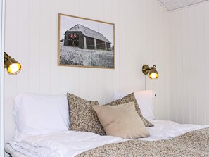 A bed with white bedding and multiple pillows, a framed picture on the wall, and two wall-mounted lamps. - 4 Star Holiday Home in Blavand (Blavand)