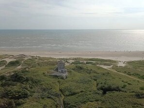 A coastal landscape with a sandy beach and a grassy area with a stone structure. - 4 Star Holiday Home in Blavand (Blavand)