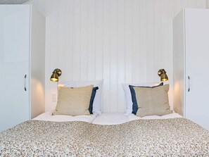 Un dormitorio con una cama centrada entre dos armarios blancos, cada uno con un tirador. Hay dos lámparas de pared a cada lado de la cama.