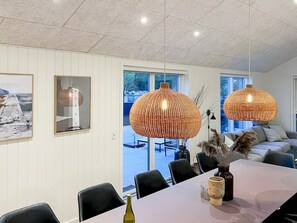 A dining area with a long table, chairs, and a bottle of wine. There are two large, round, woven pendant lights hanging above. - 4 Star Holiday Home in Blavand (Blavand)