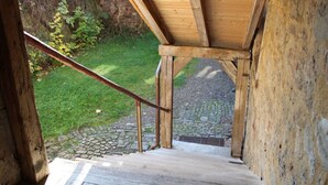 A wooden staircase leading to a covered outdoor area with a stone pathway and greenery in the background. - Pleasant Apartment in Unsleben (Unsleben)