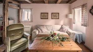 A cozy room with exposed wooden beams, a sofa with floral cushions, a wooden coffee table with a floral arrangement, and a vintage lamp. - Pleasant Apartment in Unsleben (Unsleben)
