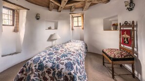 A bedroom with a wooden ceiling, a bed with a floral bedspread, a chair with a red and black patterned cushion, and a small shelf with a vase. - Pleasant Apartment in Unsleben (Unsleben)