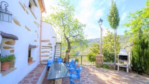 An outdoor patio with a glass table and blue chairs, surrounded by stone walls and potted plants. - Holiday Home in Laroya Near Centre (Laroya)