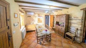 A rustic kitchen with a glass dining table, wooden cabinets, and a stone wall. - Holiday Home in Laroya Near Centre (Laroya)