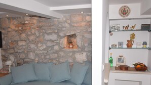 En stue med en stenvæg, en lyseblå sofa og en reol med dekorative genstande.