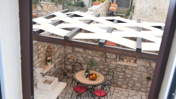 En stenbelagt terrasse med et bord og stole, en lille springvand og en pergola.