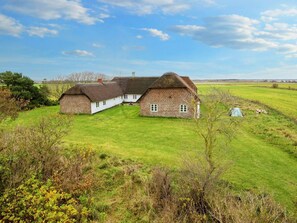 A traditional thatched-roof house with a brick extension, surrounded by a well-maintained lawn and open fields. - 9 Person Holiday Home in Tim (Tim)