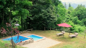 Ein Garten mit Schwimmbecken, zwei Liegestühlen und einem roten Sonnenschirm.