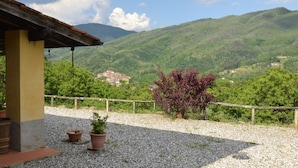 Ein Gebäude mit Kiesterrasse, Pflanzkübeln und Blick auf grüne Hügel und ein Dorf in der Ferne.