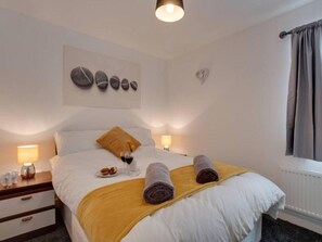 A neatly arranged bedroom with a bed, bedside lamps, a small table with a glass of wine, and a decorative wall piece. - Dirftwood Apartment in Skinningrove (Saltburn-by-the-Sea)