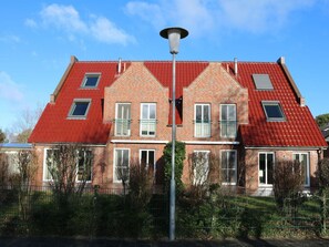 Ein zweistöckiges Backsteinhaus mit rotem Dach, zahlreichen Fenstern und einer Straßenlaterne davor.