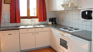 Een kleine keuken met witte kasten, een inbouwmagnetron, een fornuis en een koffiezetapparaat.