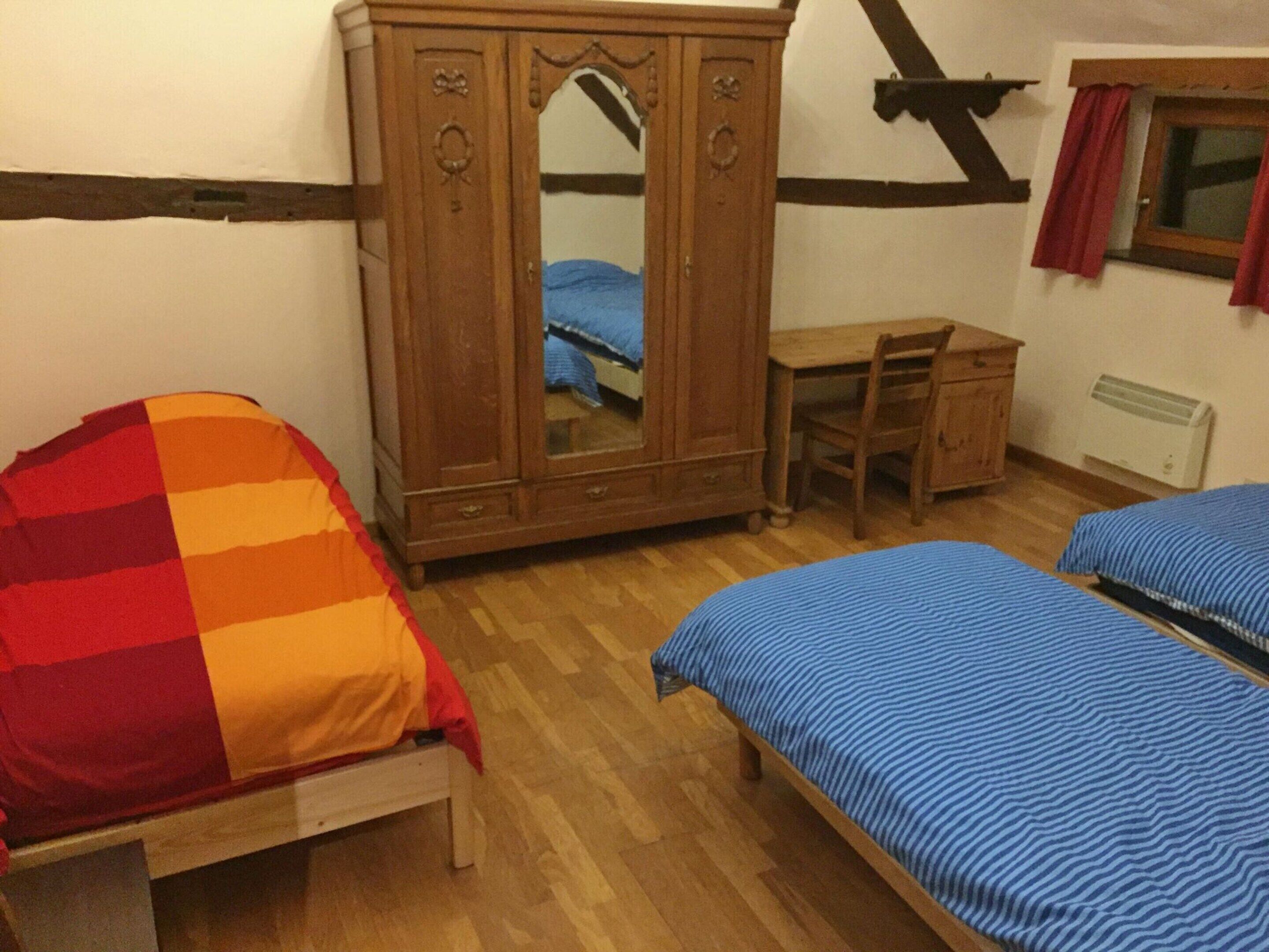 A bedroom with two single beds, a wooden wardrobe, a desk, and a window with curtains.