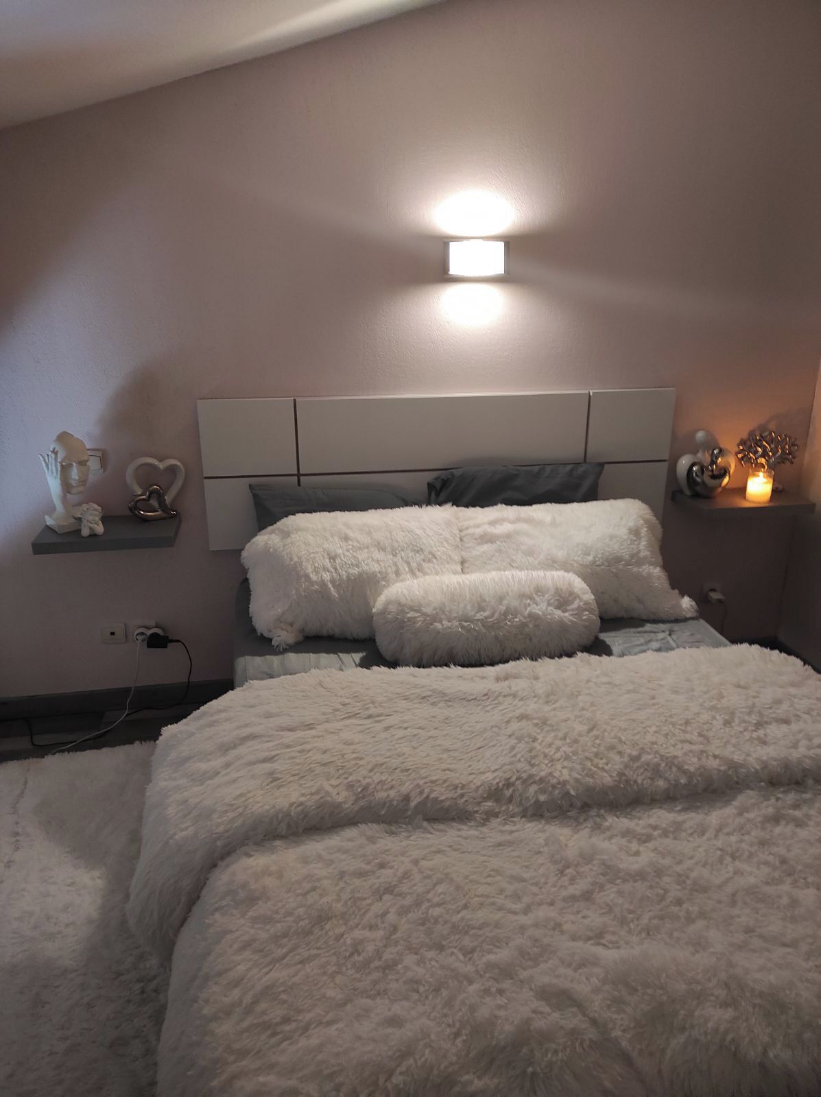 Een slaapkamer met een bed, nachtkastje, een wandlamp en decoratieve objecten.