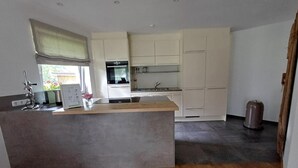 A modern kitchen with a central island, built-in appliances, and a window with a view. - Cozy Apartment in Nature (Jochberg)