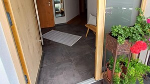 A modern entryway with a wooden door, a mirror, a small rug, and potted plants. - Cozy Apartment in Nature (Jochberg)
