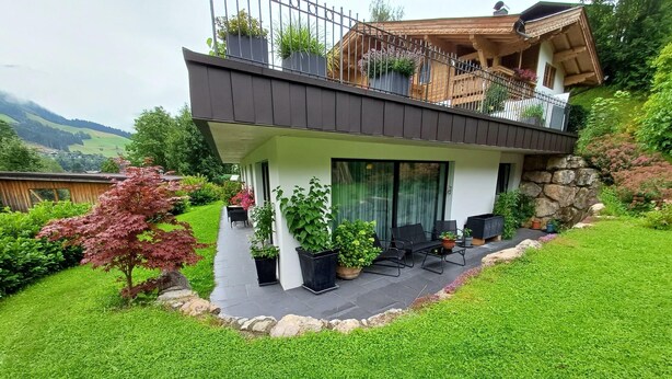 A modern two-story house with a balcony, potted plants, and a well-maintained lawn. - Cozy Apartment in Nature (Jochberg)