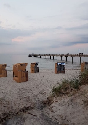 En strand med nummererede strandstole og en bro i baggrunden.