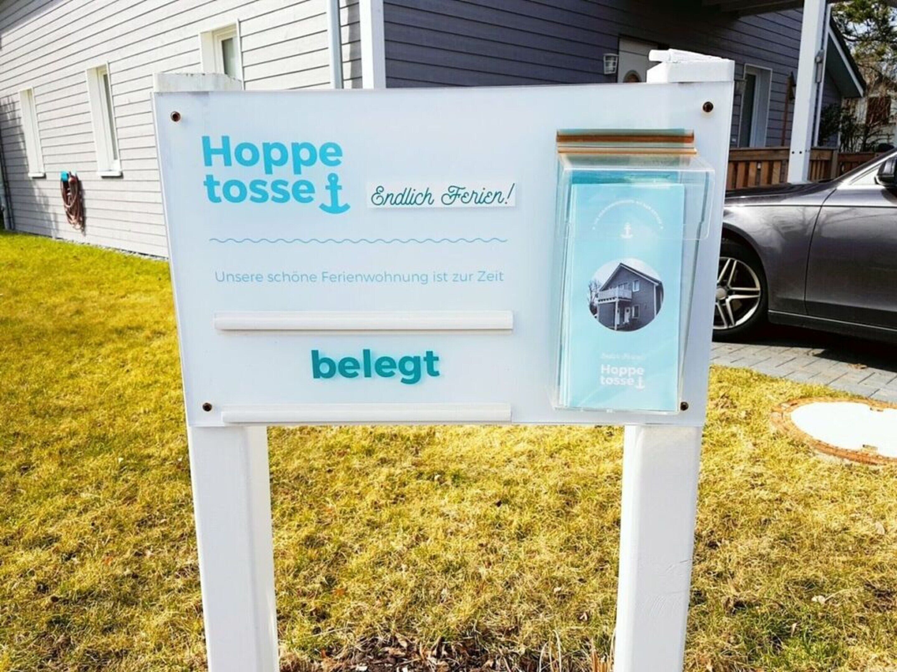 A signboard advertising a property named "Hoppe tosse" with a tagline "Endlich Ferien!" and the word "belegt" indicating availability.