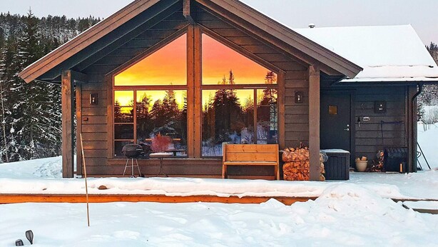 A cabin with a large window, a wooden deck, and a snow-covered ground. - 4 Star Holiday Home in Passebekk (Kongsberg)