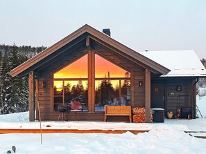 A cabin with a large window, a wooden deck, and a snow-covered ground. - 4 Star Holiday Home in Passebekk (Kongsberg)