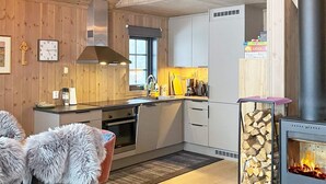 A modern kitchen with wooden walls, a built-in oven, a stove, and a dining area with a fur-covered chair. - 4 Star Holiday Home in Passebekk (Kongsberg)