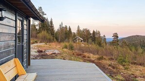 A wooden deck with a bench, overlooking a forested area with a house in the background. - 4 Star Holiday Home in Passebekk (Kongsberg)