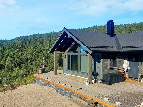 A modern cabin with a large glass door, a deck, and a view of a forested hillside. - 4 Star Holiday Home in Passebekk (Kongsberg)