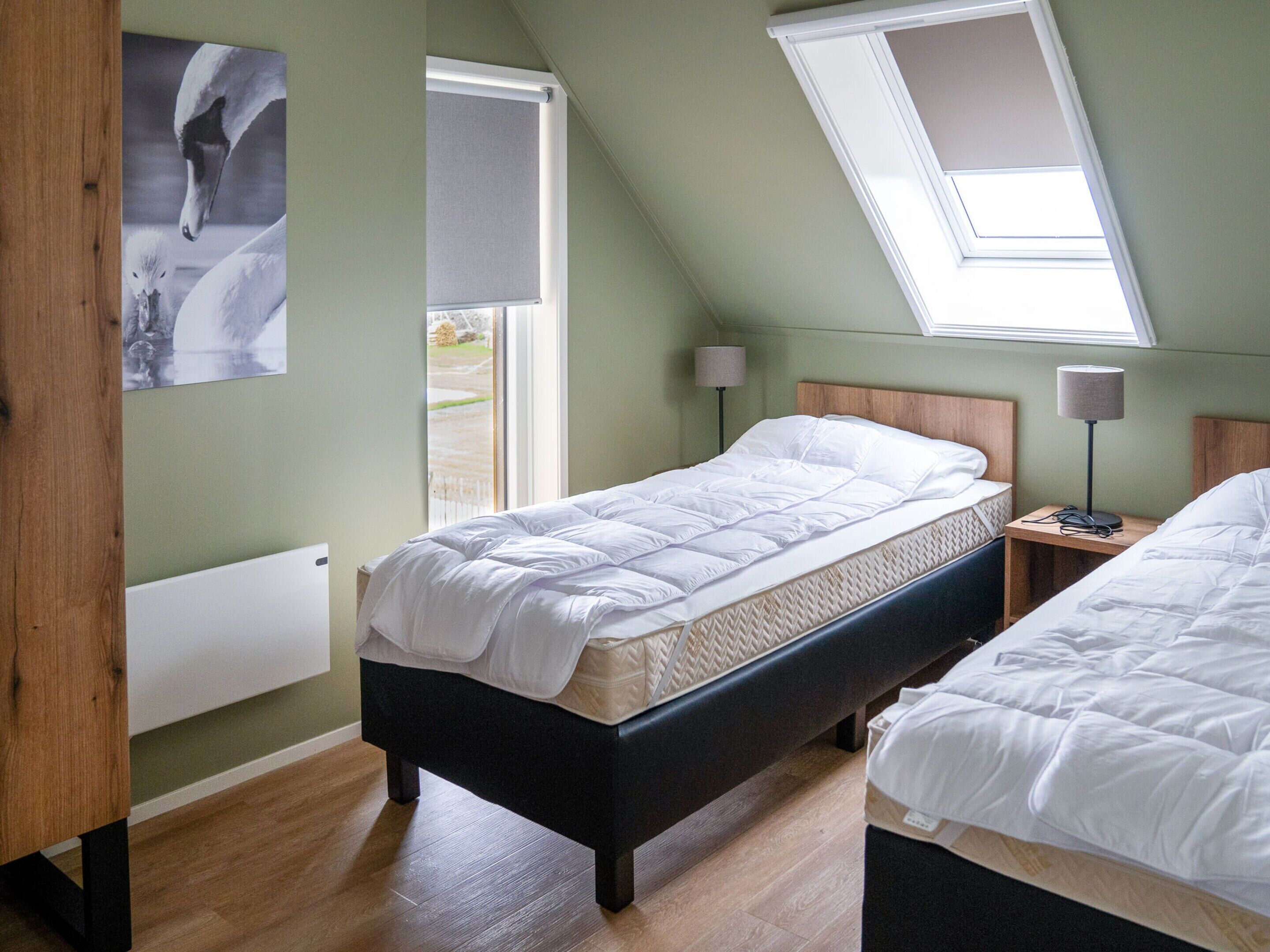 A bedroom with a sloped ceiling, a bed, a bedside table with a lamp, and a window with a view of the outdoors.