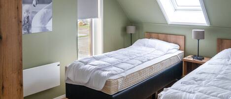 A bedroom with a sloped ceiling, a bed, a bedside table with a lamp, and a window with a view of the outdoors.