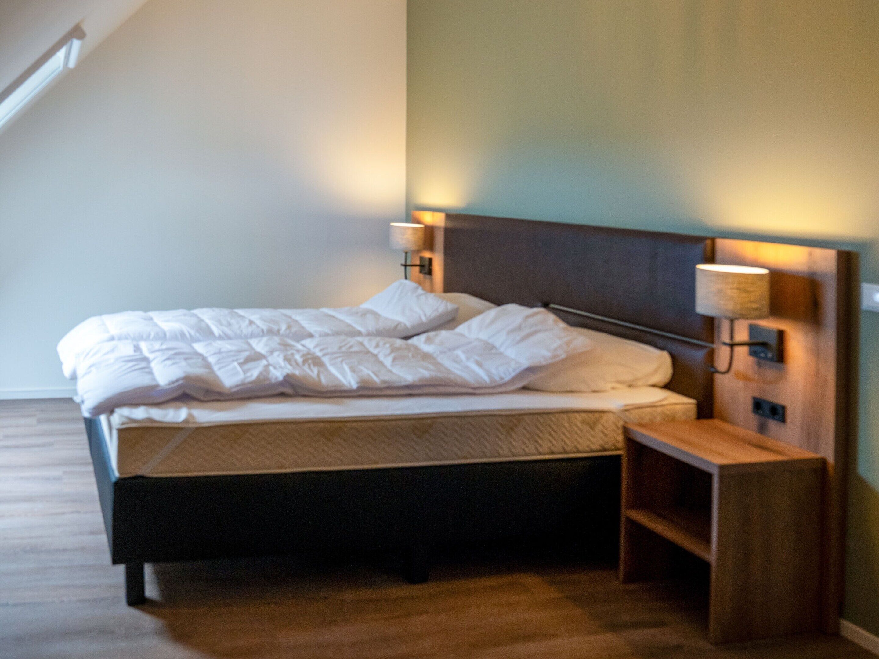 A neatly made bed with a wooden headboard and two bedside lamps.