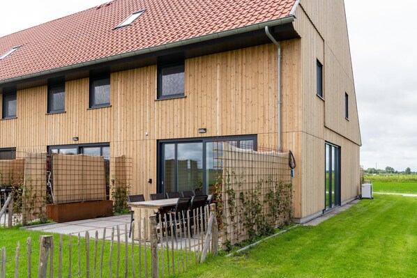 A modern building with a wooden facade, large windows, and a fenced outdoor area with a table and chairs.